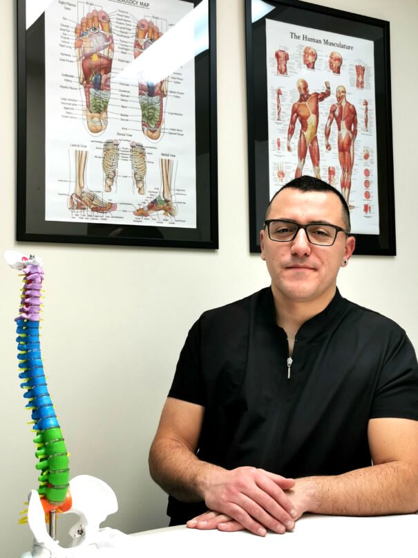 Fotografía Retrato de Víctor Flores en su clínica con cuadros técnicos del cuerpo humano de fondo